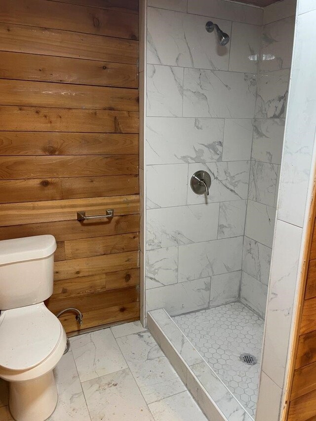 bathroom with wood walls, toilet, and a tile shower