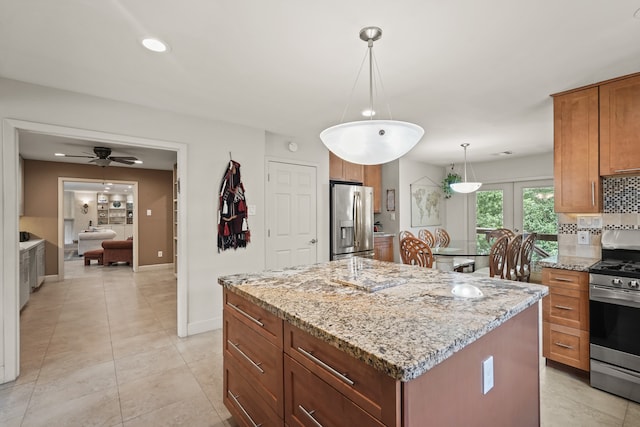 kitchen with a kitchen island, pendant lighting, stainless steel appliances, ceiling fan, and light stone counters