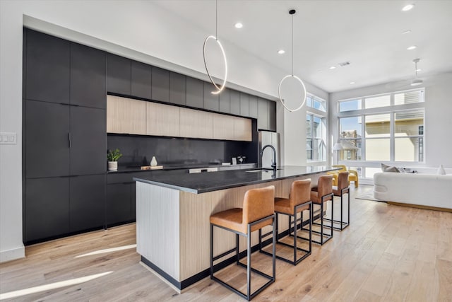 kitchen with a large island with sink, light wood-type flooring, decorative light fixtures, decorative backsplash, and a breakfast bar area