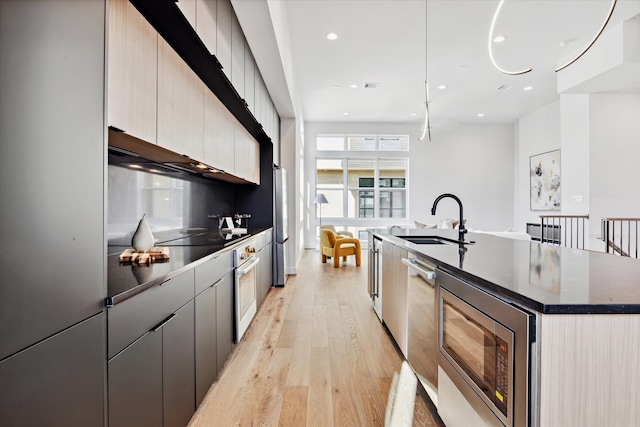 kitchen with hanging light fixtures, a center island with sink, light wood-type flooring, stainless steel appliances, and sink