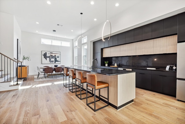 kitchen featuring backsplash, hanging light fixtures, light hardwood / wood-style flooring, light brown cabinets, and a kitchen island with sink