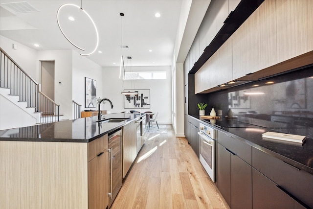 kitchen featuring a large island, oven, light hardwood / wood-style flooring, sink, and decorative light fixtures