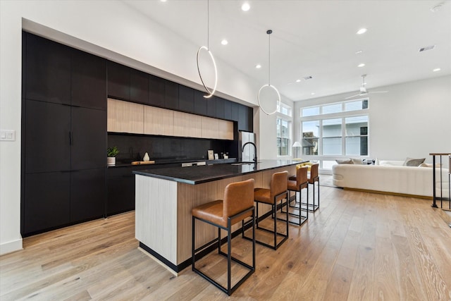 kitchen featuring pendant lighting, sink, a kitchen breakfast bar, a kitchen island with sink, and light wood-type flooring