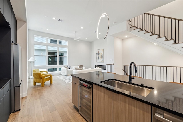 kitchen featuring pendant lighting, sink, stainless steel refrigerator, beverage cooler, and light wood-type flooring