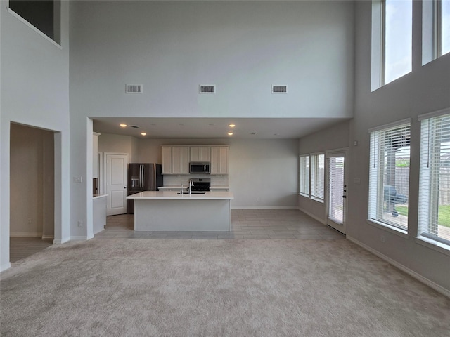 unfurnished living room featuring light carpet, sink, and a towering ceiling