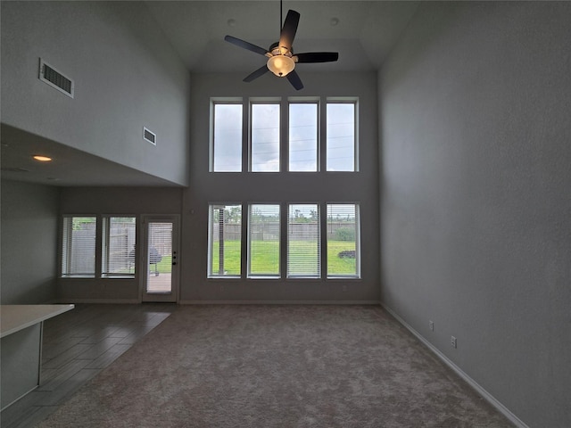 unfurnished living room featuring dark carpet, a wealth of natural light, ceiling fan, and a high ceiling