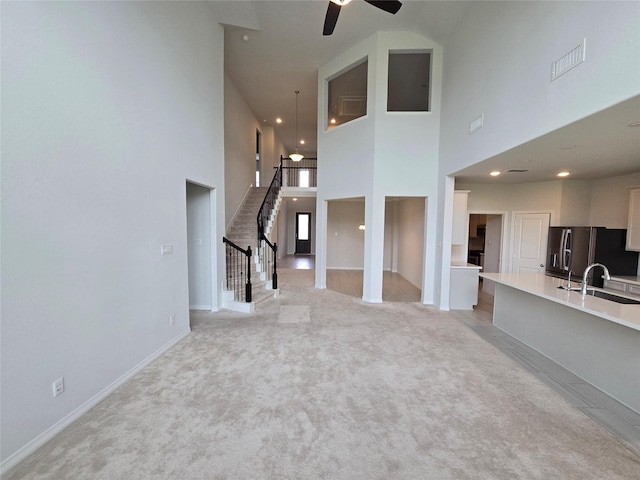 unfurnished living room featuring sink, light colored carpet, ceiling fan, and a high ceiling