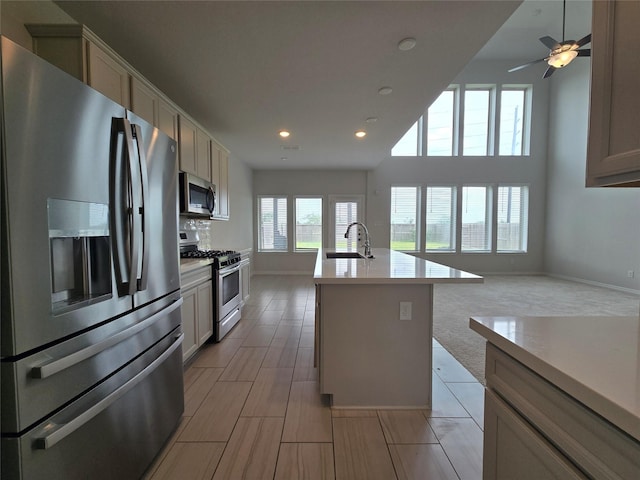 kitchen featuring appliances with stainless steel finishes, a kitchen island with sink, sink, and ceiling fan