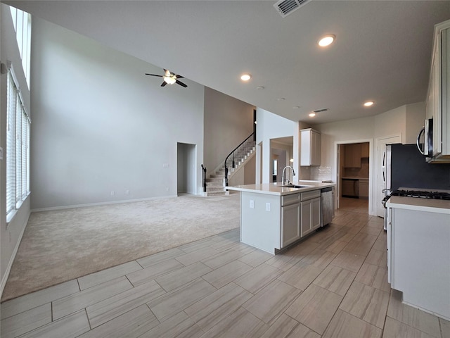 kitchen featuring sink, ceiling fan, appliances with stainless steel finishes, a kitchen island with sink, and light carpet