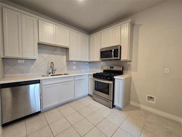 kitchen with sink, tasteful backsplash, light tile patterned floors, appliances with stainless steel finishes, and white cabinets