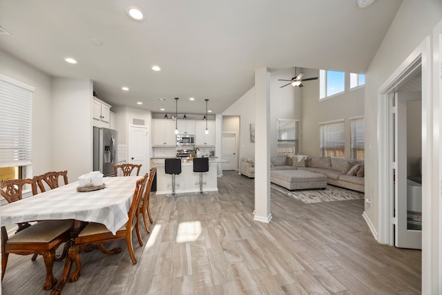 dining space featuring ceiling fan, light hardwood / wood-style flooring, and a towering ceiling