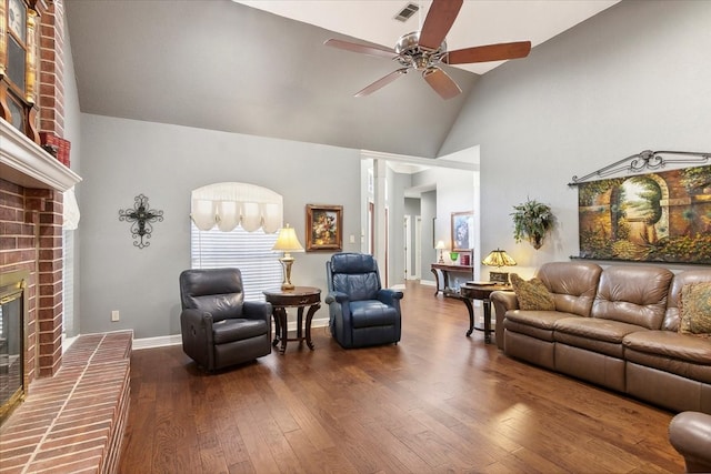 living room featuring lofted ceiling, dark wood-type flooring, a brick fireplace, ceiling fan, and brick wall