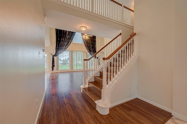 stairway featuring ceiling fan, a towering ceiling, and hardwood / wood-style flooring