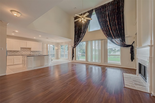 unfurnished living room with sink, high vaulted ceiling, a fireplace, ceiling fan with notable chandelier, and light wood-type flooring