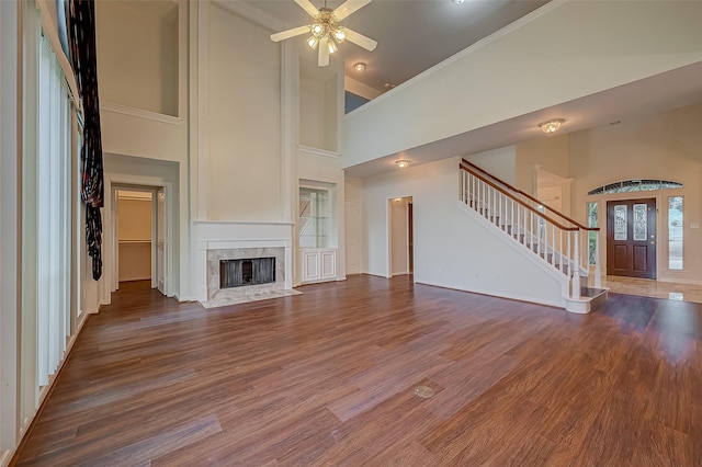 unfurnished living room featuring a premium fireplace, a towering ceiling, dark wood-type flooring, and ceiling fan