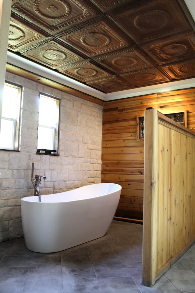 bathroom with tile patterned floors, coffered ceiling, wood walls, and a bath