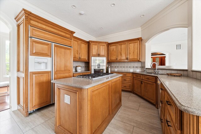 kitchen with decorative backsplash, sink, light tile patterned floors, stainless steel appliances, and a kitchen island