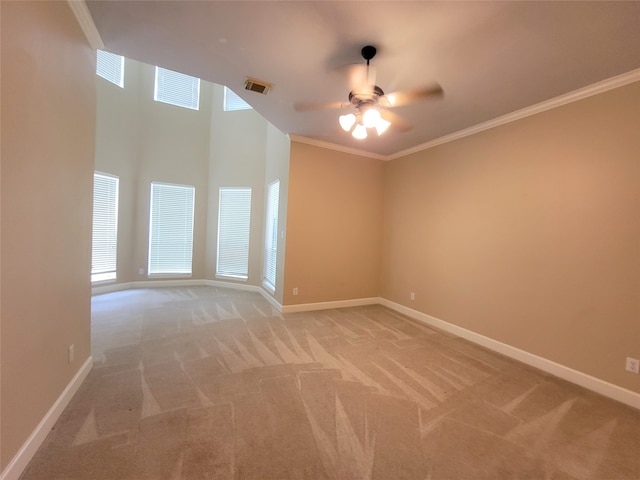 carpeted spare room with ceiling fan, a towering ceiling, plenty of natural light, and ornamental molding