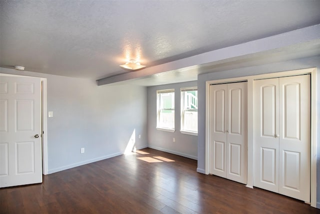 unfurnished bedroom featuring a textured ceiling, dark hardwood / wood-style flooring, and two closets