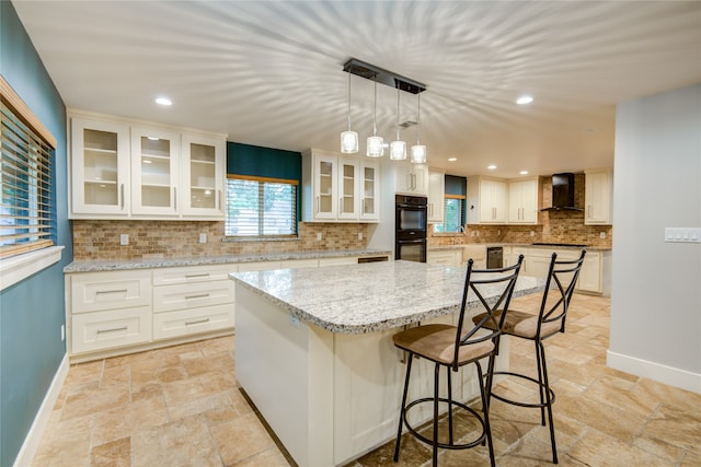 kitchen with a kitchen bar, backsplash, wall chimney exhaust hood, and white cabinetry