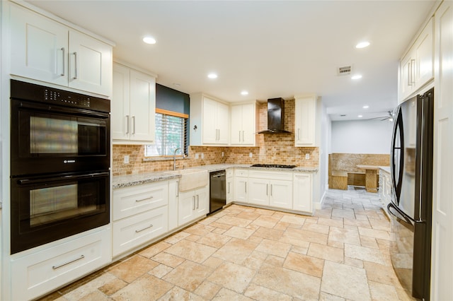 kitchen with light stone countertops, black appliances, sink, wall chimney range hood, and white cabinets