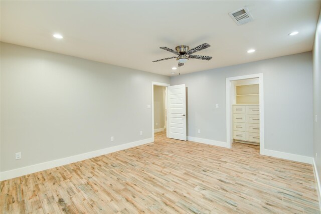 unfurnished bedroom with ceiling fan, a walk in closet, a closet, and light hardwood / wood-style floors