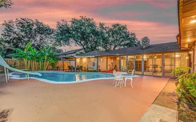 pool at dusk with a water slide and a patio