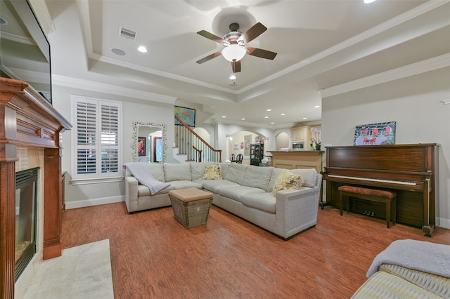 living room with a raised ceiling, a fireplace, crown molding, light hardwood / wood-style floors, and ceiling fan