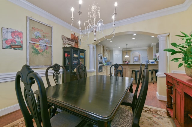 dining room featuring a notable chandelier, crown molding, light wood-type flooring, and ornate columns