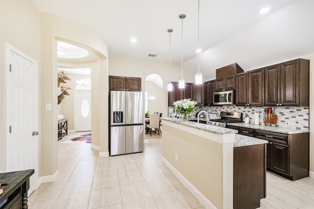 kitchen featuring stainless steel appliances, hanging light fixtures, light stone countertops, a center island with sink, and tasteful backsplash