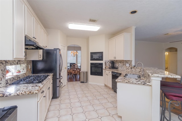 kitchen with visible vents, a peninsula, under cabinet range hood, arched walkways, and black appliances