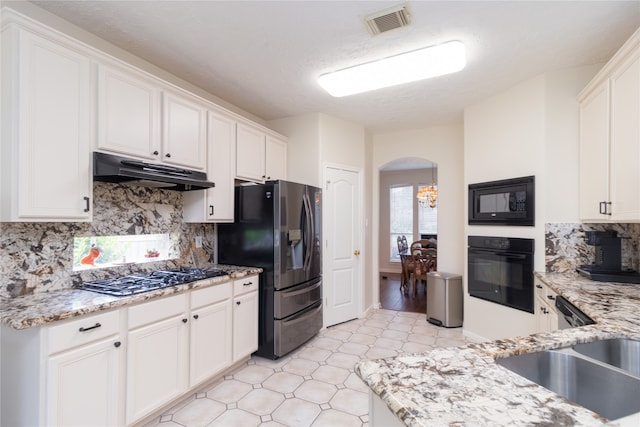 kitchen featuring decorative backsplash, light stone counters, white cabinets, black appliances, and light tile patterned floors