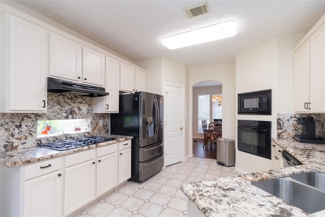 kitchen with under cabinet range hood, white cabinets, light stone counters, arched walkways, and black appliances