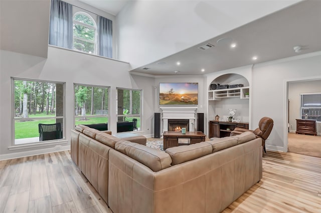 living room with built in shelves, crown molding, a high ceiling, and light hardwood / wood-style flooring