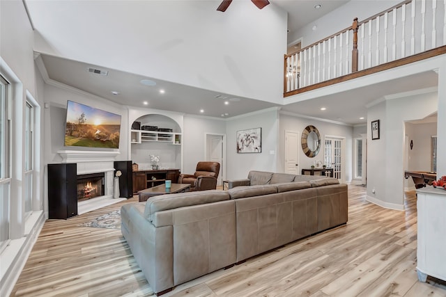 living room with plenty of natural light, light wood-type flooring, crown molding, and a high ceiling