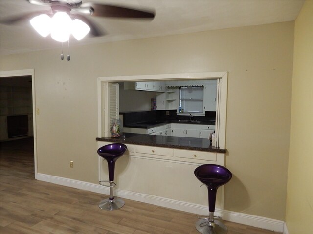 kitchen with a kitchen bar, sink, ceiling fan, and light hardwood / wood-style floors