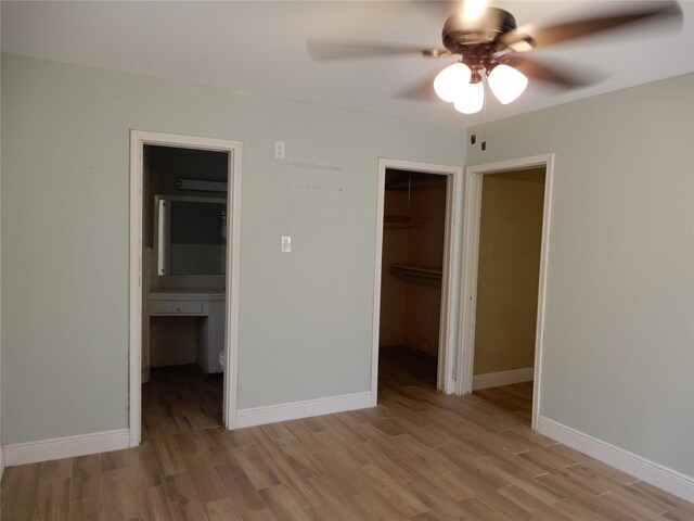 unfurnished bedroom with ceiling fan, hardwood / wood-style flooring, a walk in closet, connected bathroom, and a closet