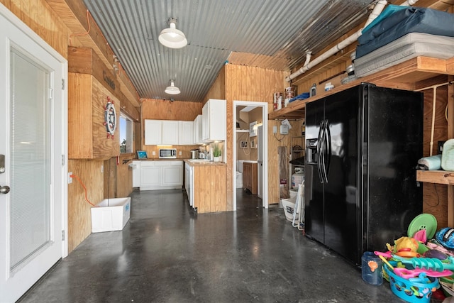 kitchen with wood walls, black fridge with ice dispenser, white cabinets, finished concrete flooring, and stainless steel microwave