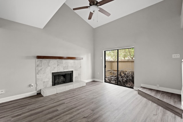 unfurnished living room with ceiling fan, high vaulted ceiling, a tiled fireplace, and wood-type flooring