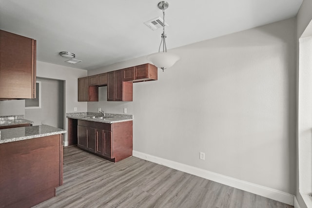 kitchen with sink, decorative light fixtures, light hardwood / wood-style flooring, and light stone counters