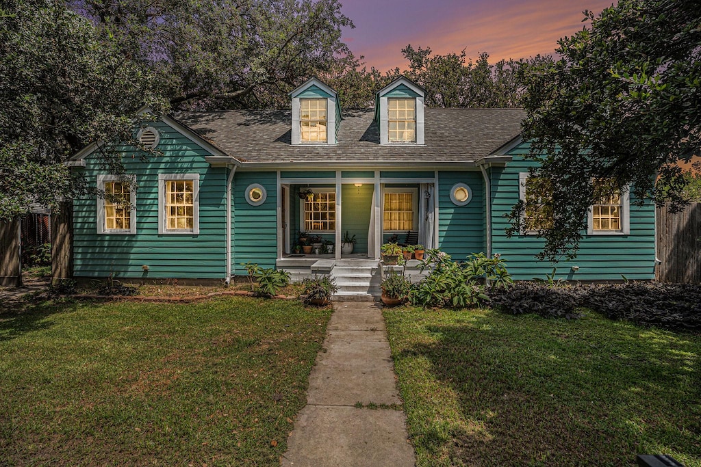 new england style home featuring roof with shingles, a porch, and a yard