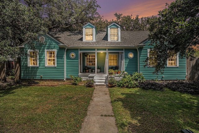 new england style home featuring roof with shingles, a porch, and a yard