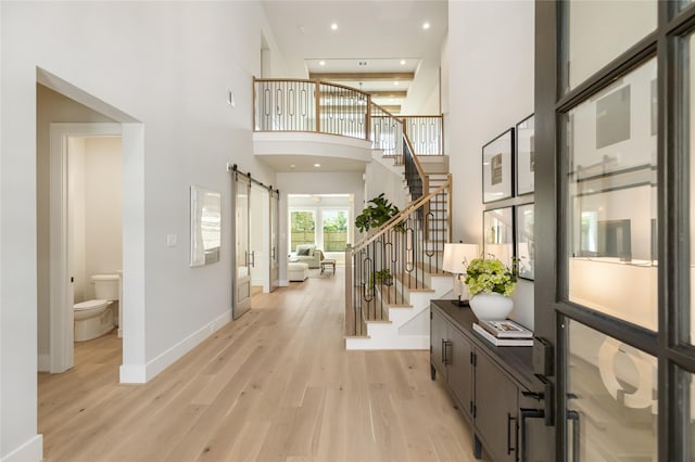 foyer entrance with a barn door, a towering ceiling, and light hardwood / wood-style flooring