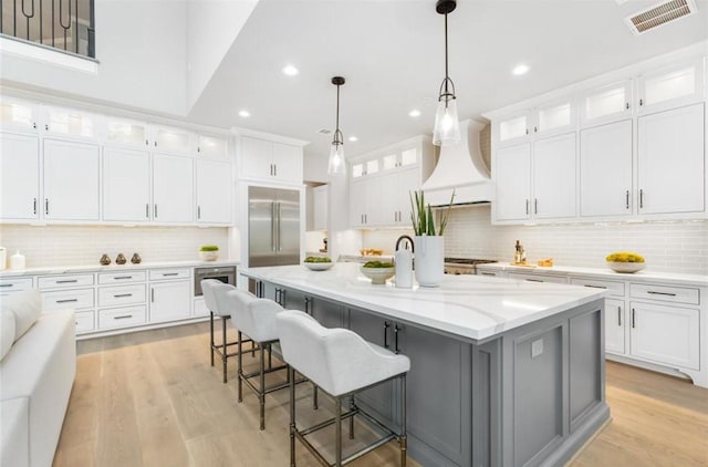 kitchen with white cabinets, custom exhaust hood, a spacious island, and built in refrigerator