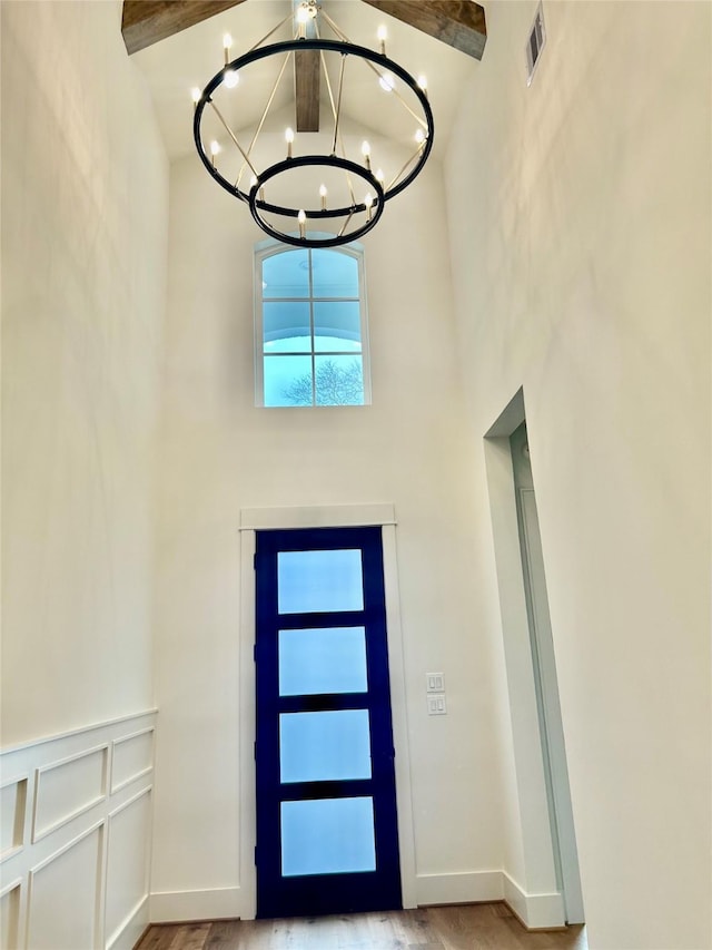 entryway with wood finished floors, baseboards, visible vents, a high ceiling, and a chandelier