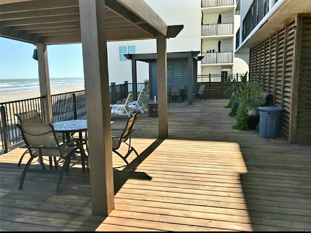 wooden terrace with a water view, outdoor dining space, and a beach view