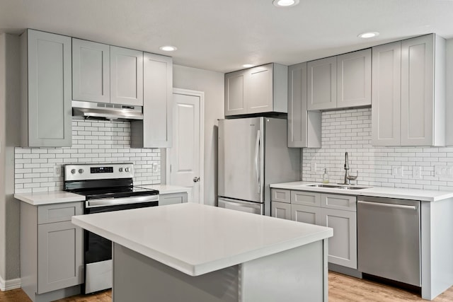 kitchen with appliances with stainless steel finishes, sink, light wood-type flooring, and a kitchen island