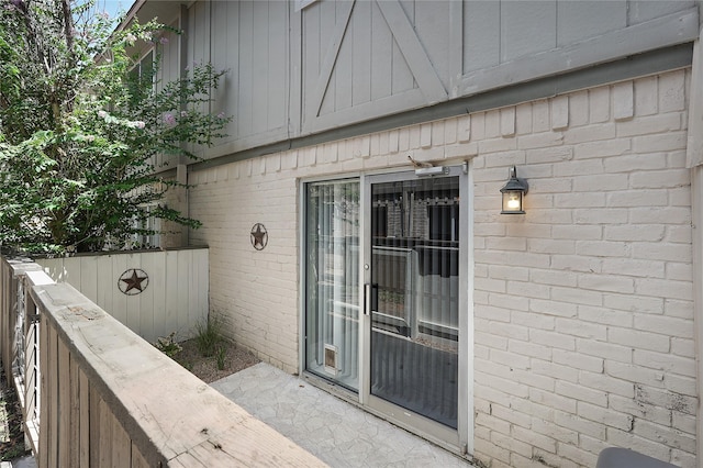 view of exterior entry with fence and brick siding