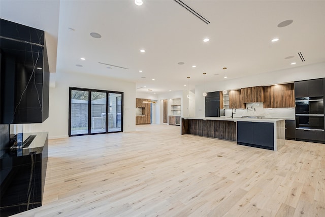 kitchen with a large island, black double oven, light hardwood / wood-style floors, decorative light fixtures, and stainless steel gas stovetop