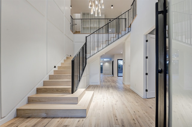 staircase featuring hardwood / wood-style floors, a towering ceiling, and an inviting chandelier